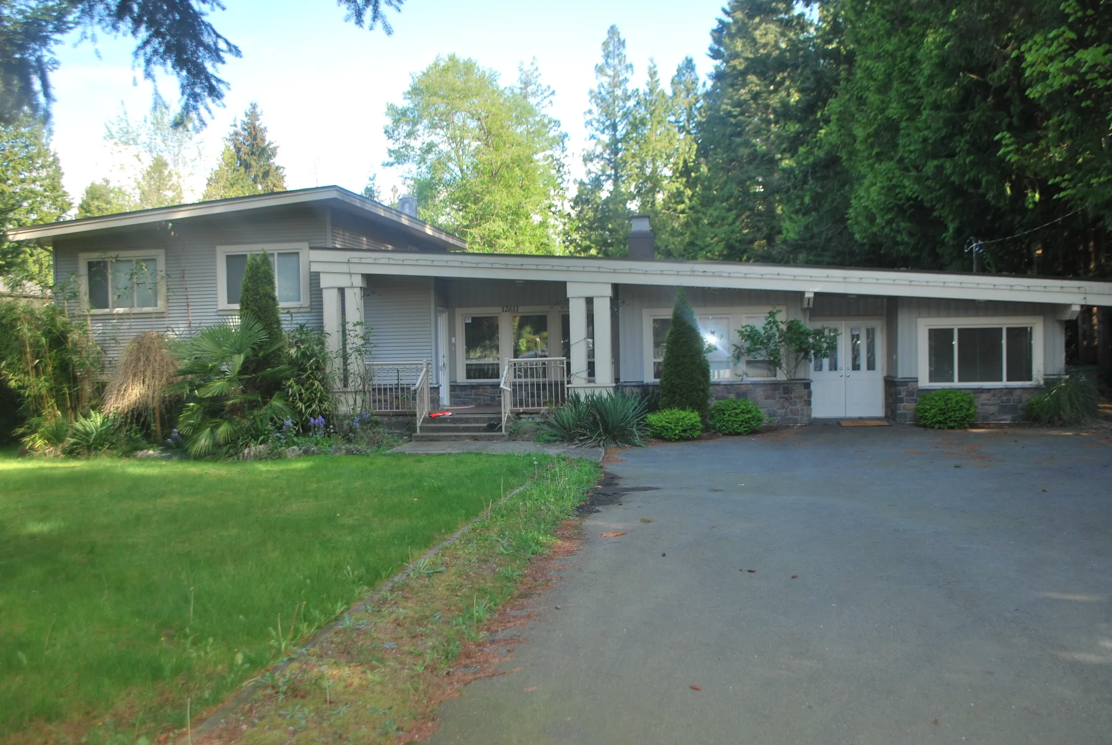 Pre-renovation front exterior, dated grey siding home with covered porch, white columns, and stone accents.