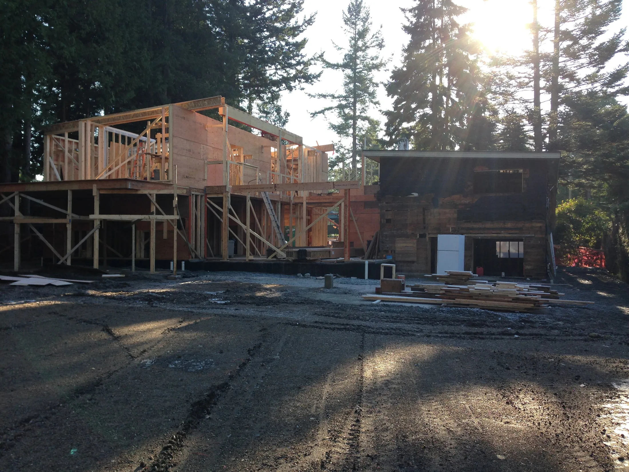 Framing stage: new second-story wood framing rises above the original structure at sunrise, lumber staged below.
