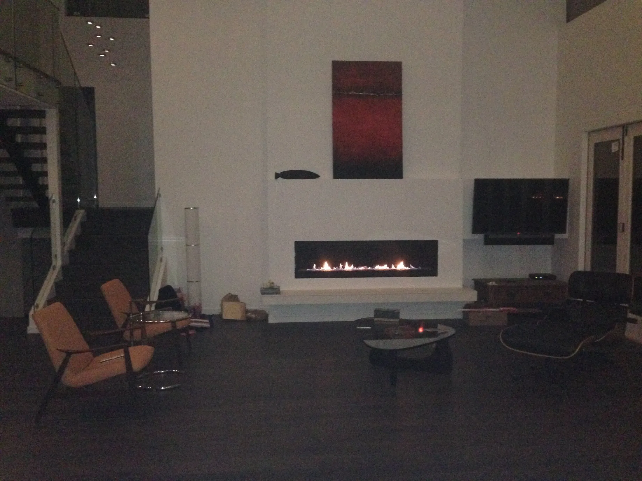 Living room with linear gas fireplace, mounted TV, red abstract art, and open wood staircase.