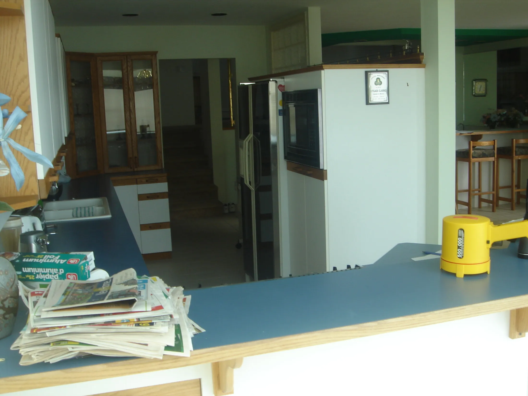 Original kitchen and hallway with stainless fridge, built-in microwave, blue laminate counters, and glass-front oak cabinets.