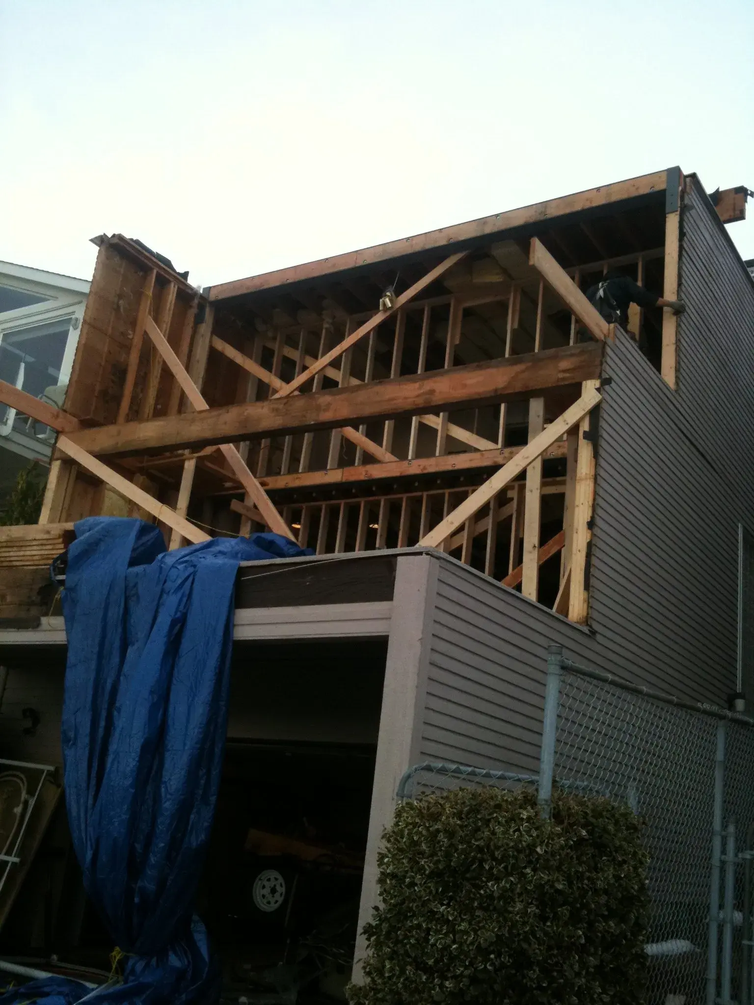 Mid-demolition view of the exposed roof framing and rafters, stripped siding, and a blue tarp below.