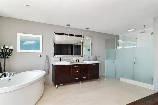 Ensuite bathroom with a dark wood double vanity, freestanding oval tub, and frameless glass corner shower.