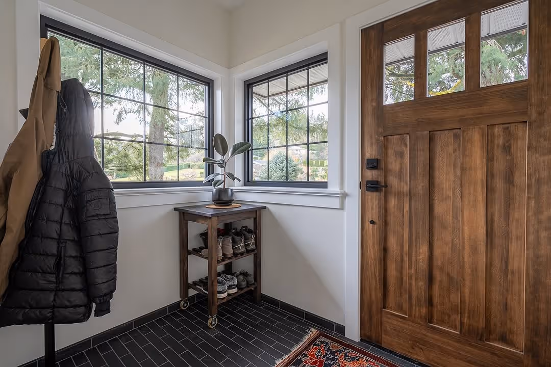 Entryway with dark stained oak front door, corner windows, and wheeled wood shoe bench.