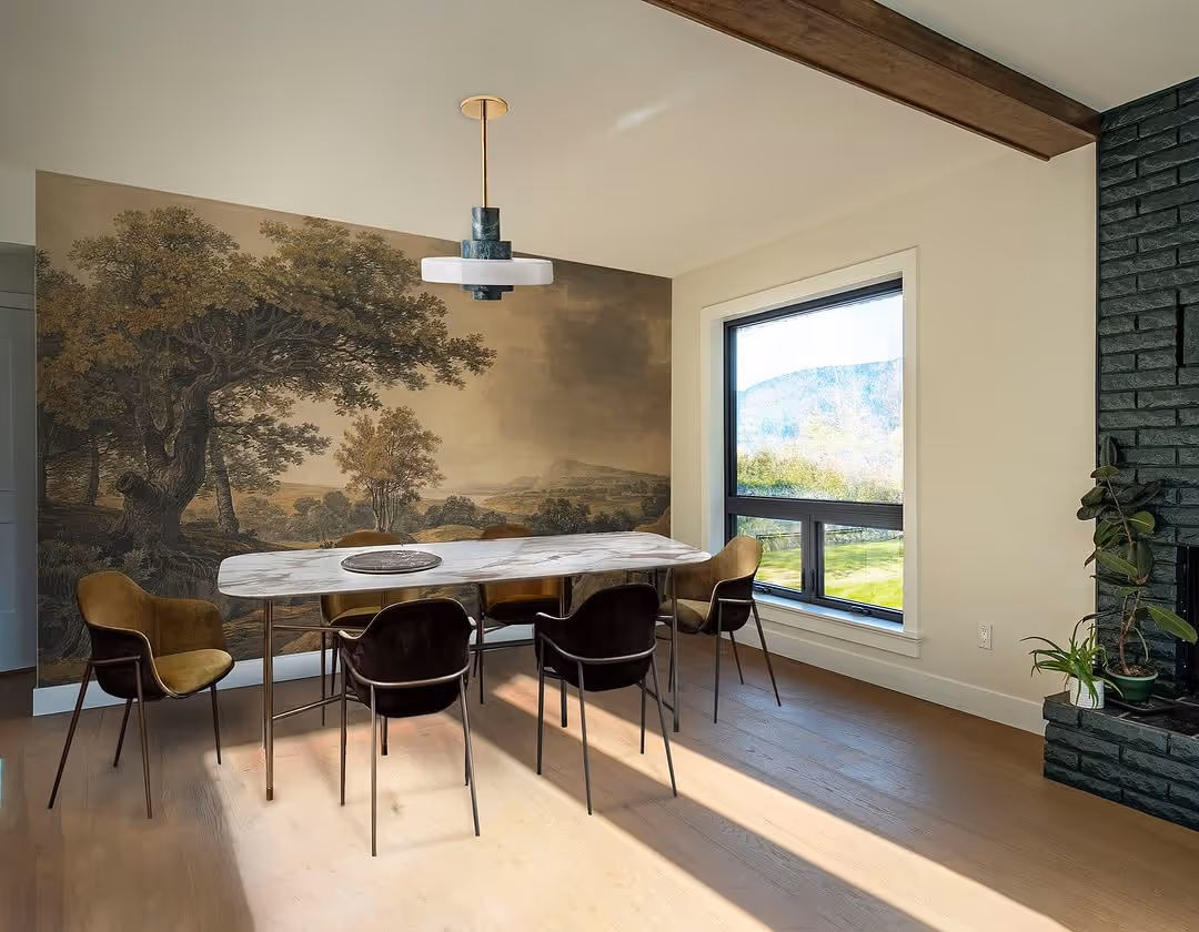 Dining area with oversized landscape mural, marble table, mixed velvet chairs, and exposed wood beam.
