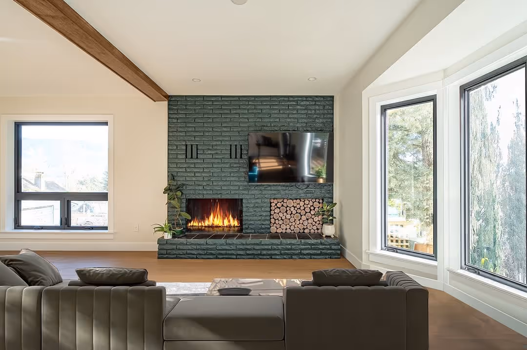 Living room with sage-green painted brick fireplace, lit fire, built-in wood storage, and wraparound windows.