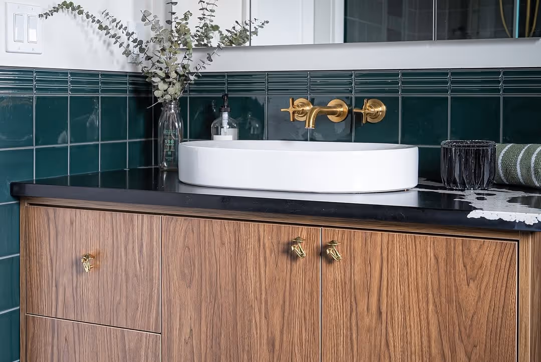 Bathroom vanity with walnut cabinetry, black stone counter, oval vessel sink, and brass wall-mount faucet.
