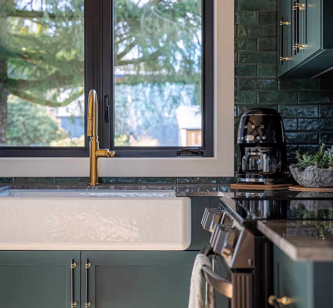 Kitchen sink area with farmhouse sink, brass gooseneck faucet, black casement window, and Smeg coffee maker.