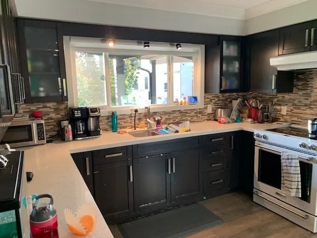 Original kitchen before renovation, with dark wood cabinets, mosaic tile backsplash, and worn laminate counters.