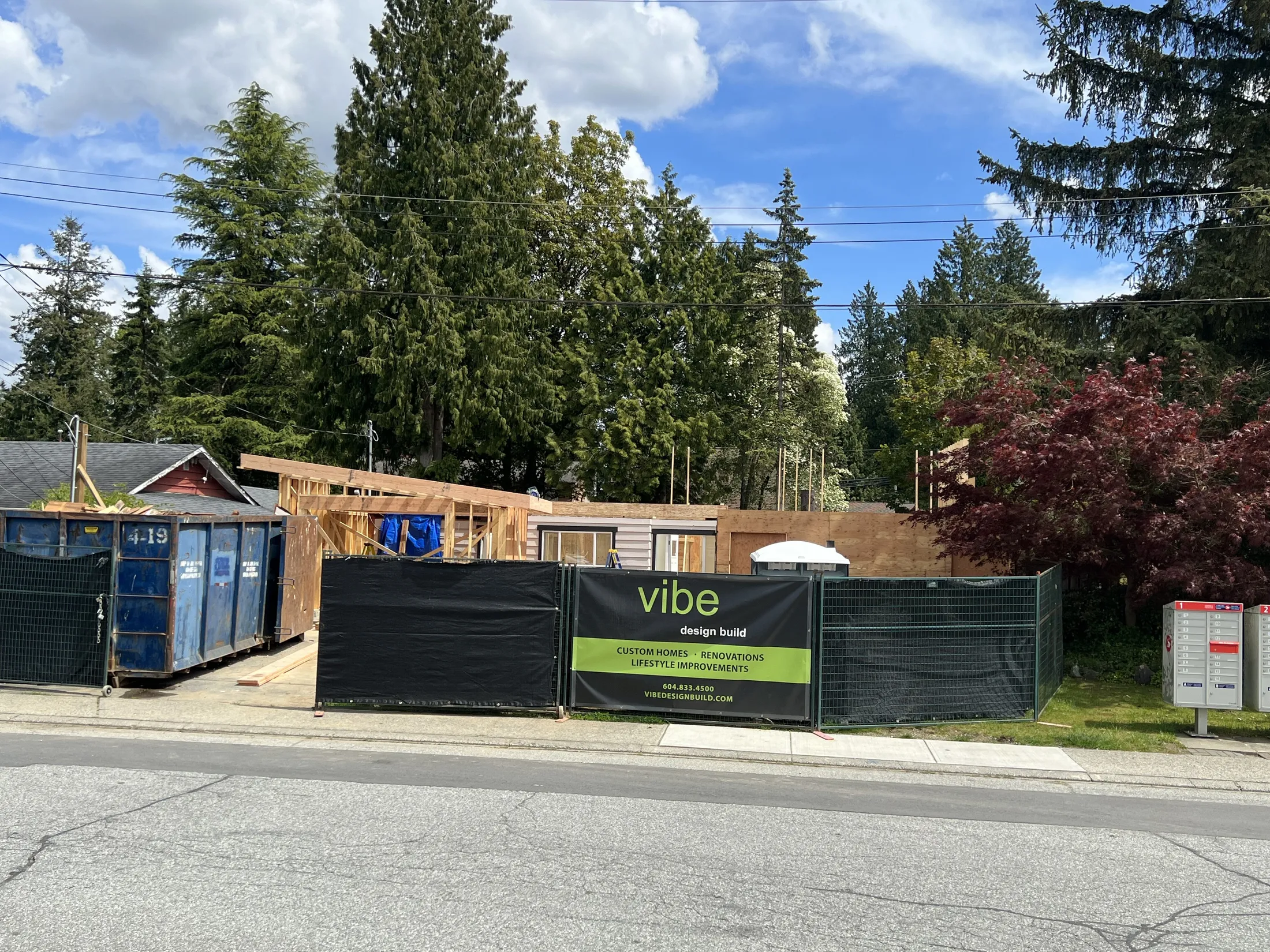 Mid-construction exterior behind site fencing, showing the new wood-framed addition and dumpster during the rebuild.