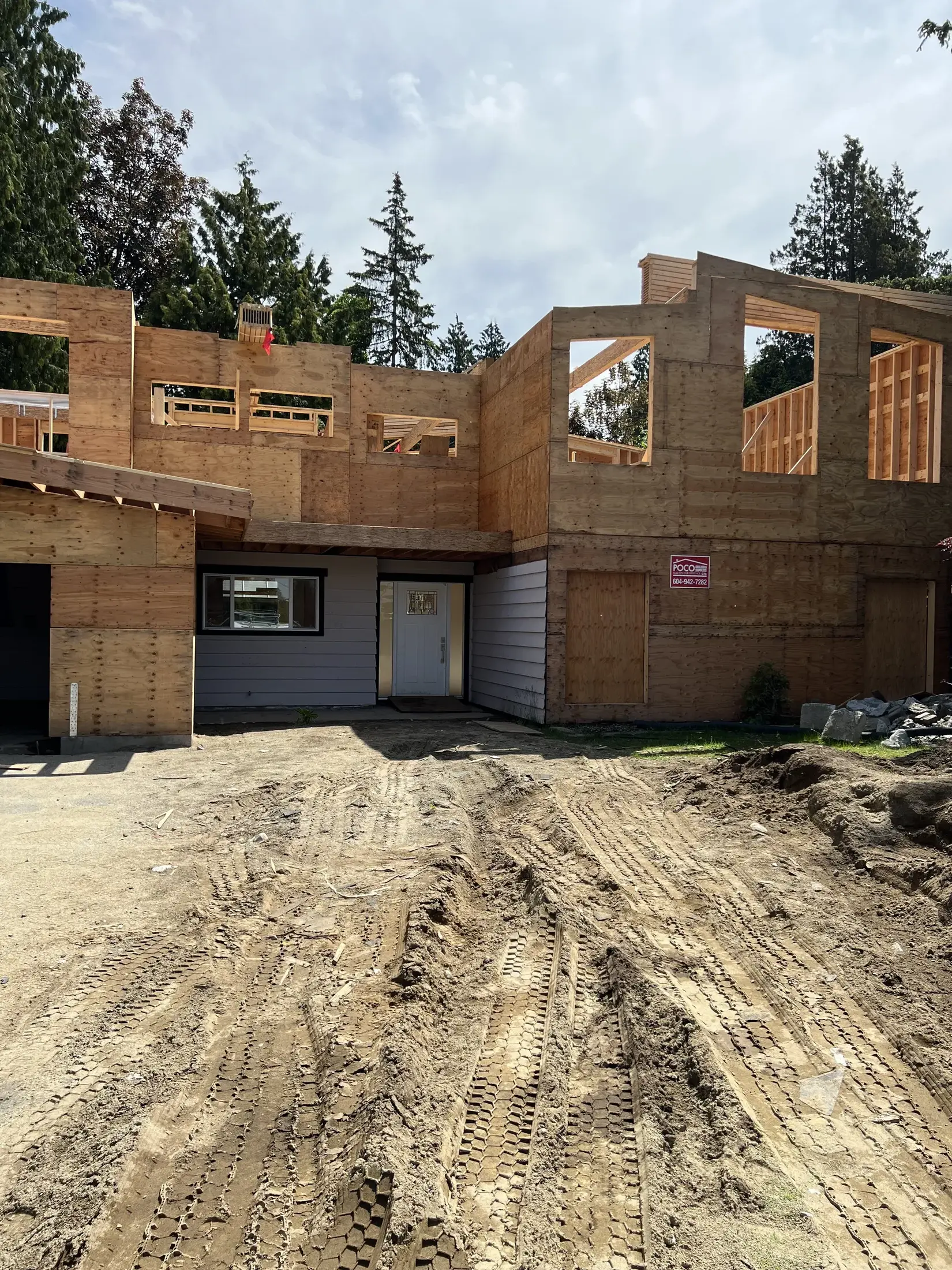 Mid-construction front view of the fully framed home, plywood-sheathed with window and door openings cut.