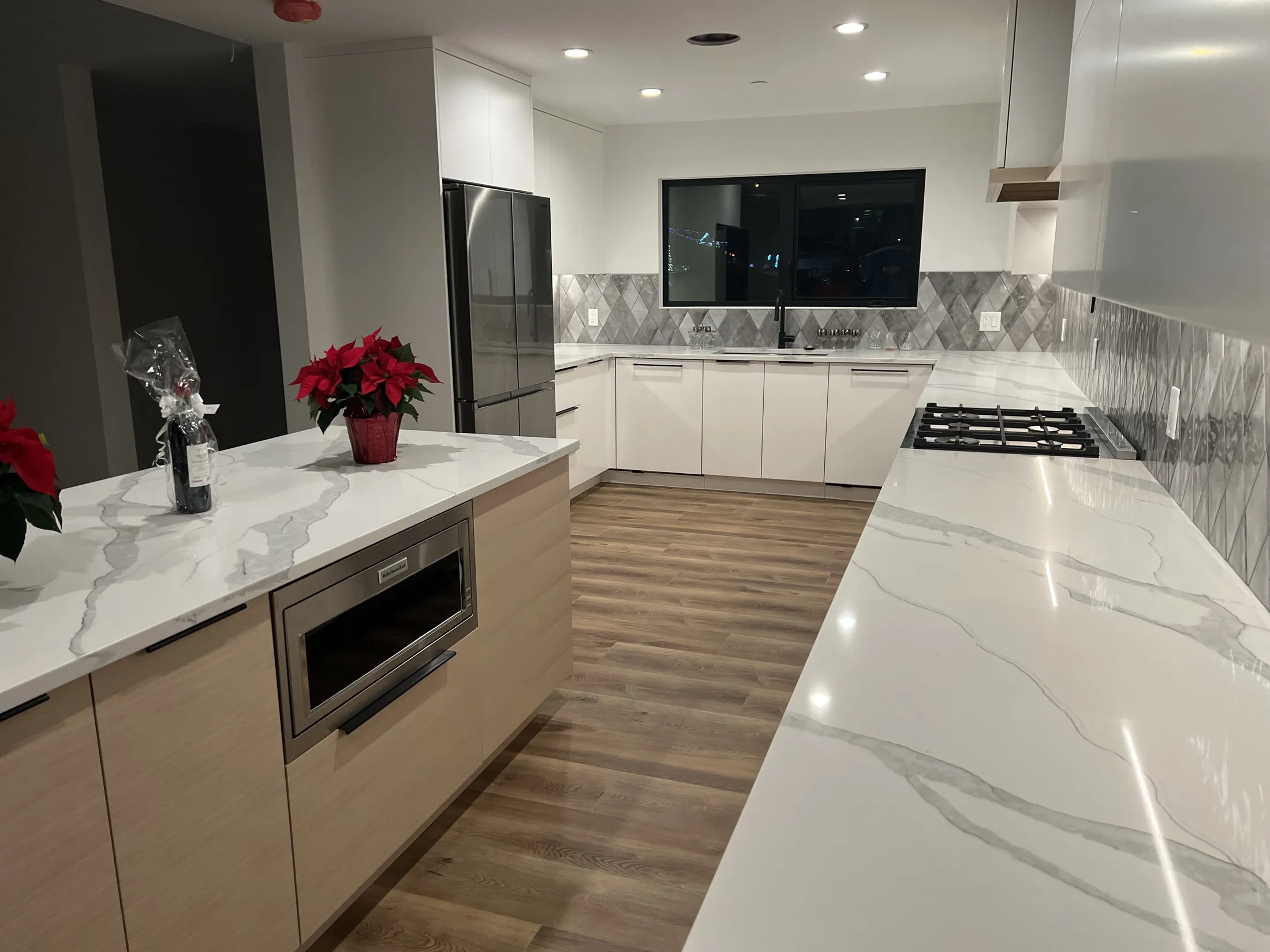 Wide kitchen view with wood-tone island, stainless fridge, waterfall quartz counters, and window over sink.