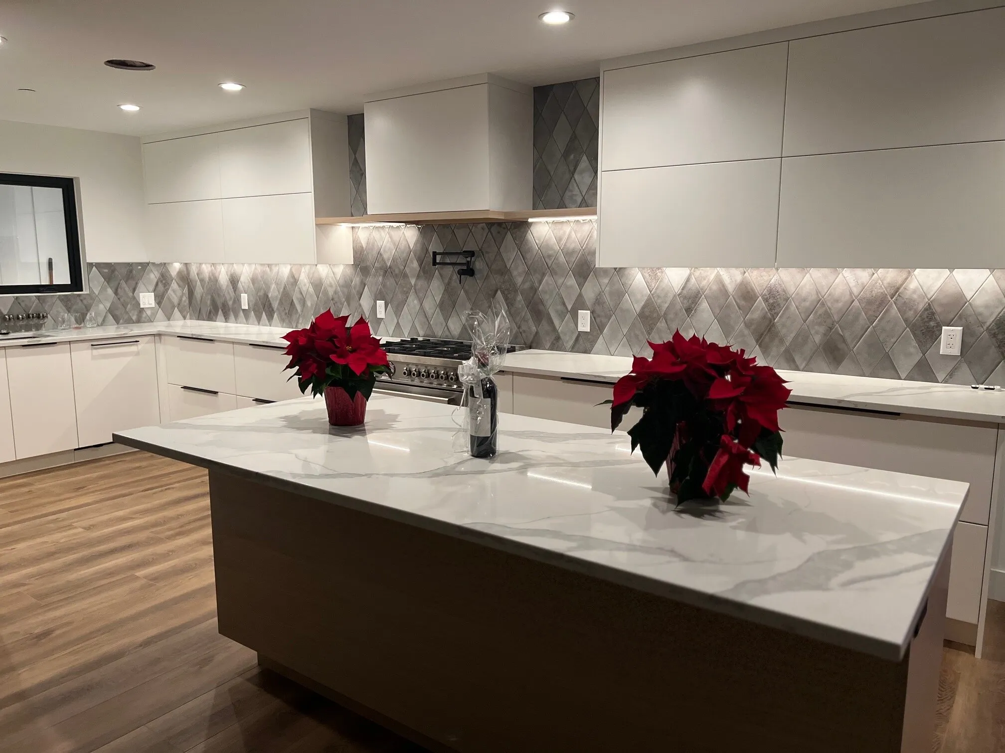 Island with waterfall quartz countertop and poinsettias, overlooking the range and diamond-tile backsplash beyond.