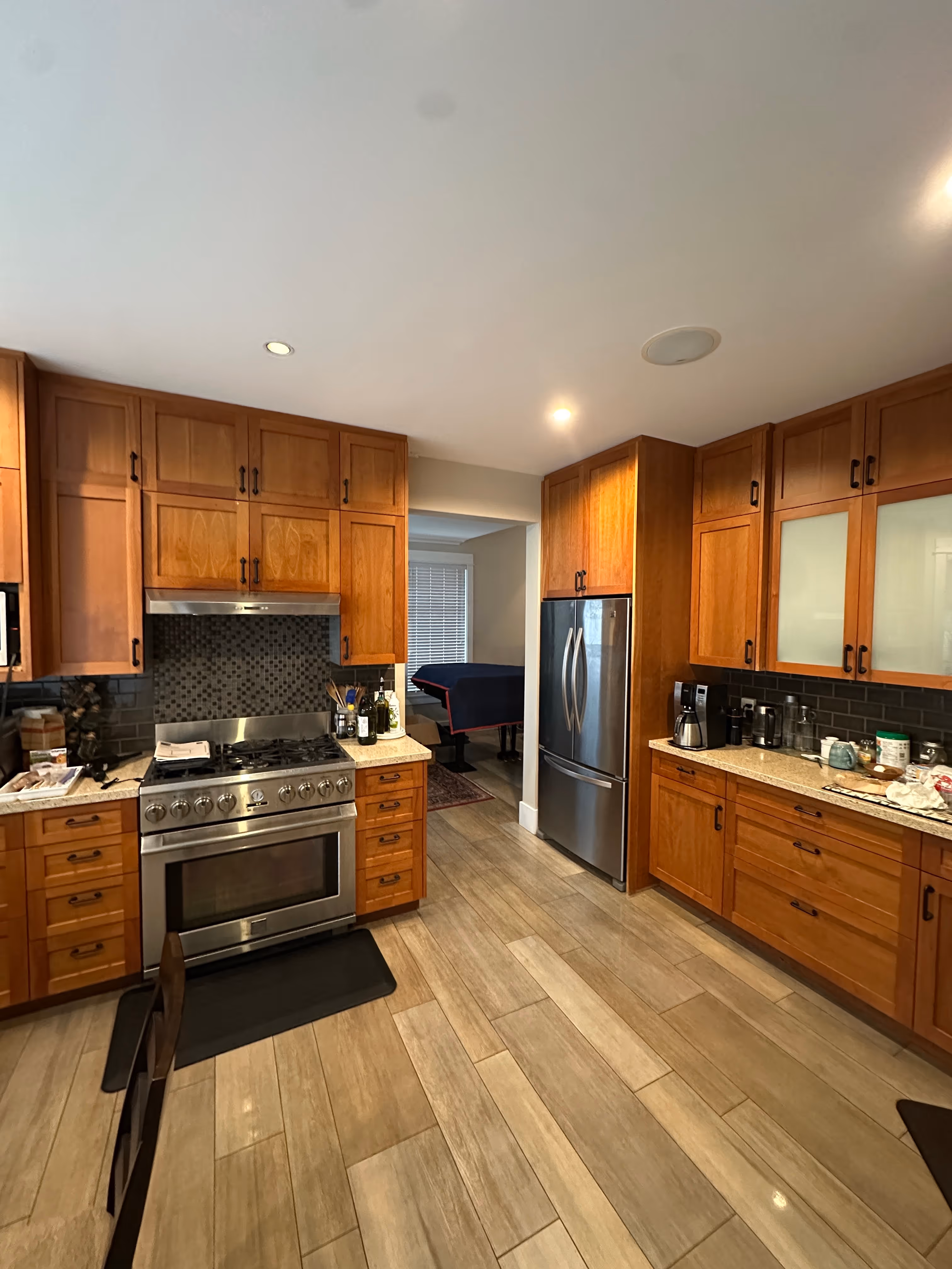 Dated honey-oak kitchen with mosaic tile backsplash, gas range, and cluttered laminate counters before renovation.