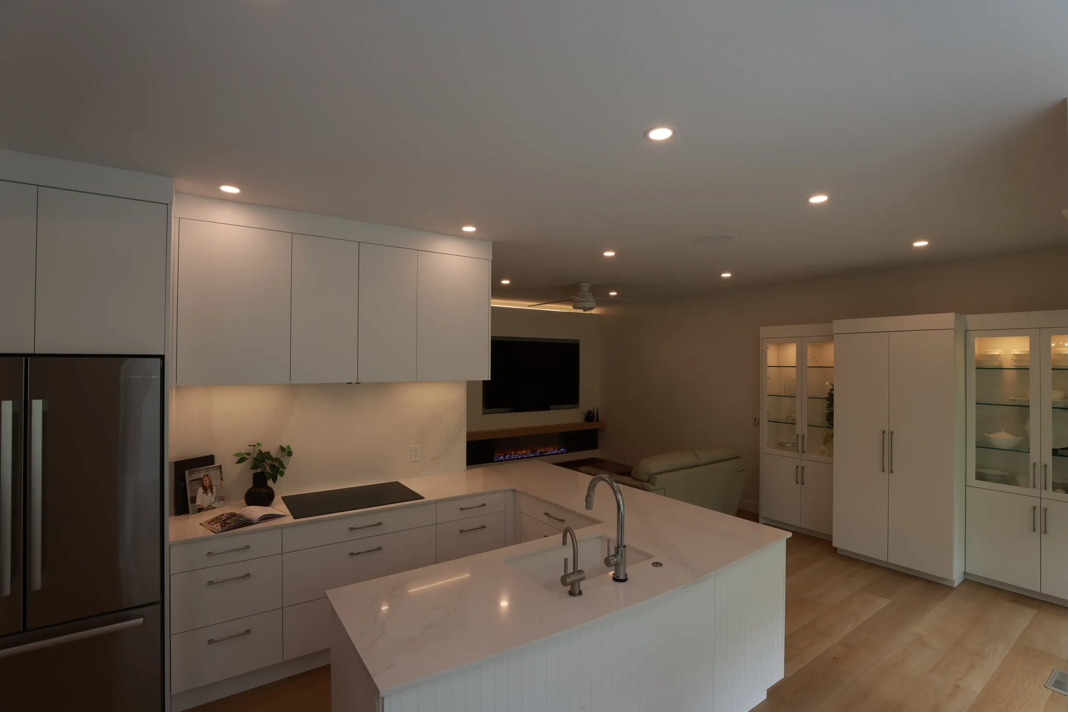 Kitchen island countertop leads toward the ceiling fan and built-in fireplace and TV wall.