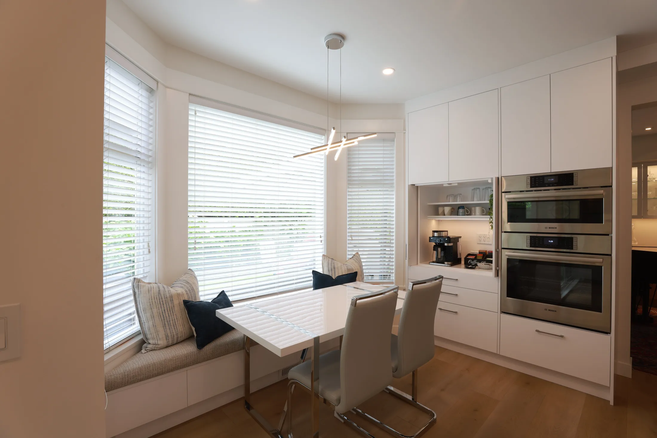 Window-seat breakfast nook with striped cushions sits beside the open coffee bar cabinet.
