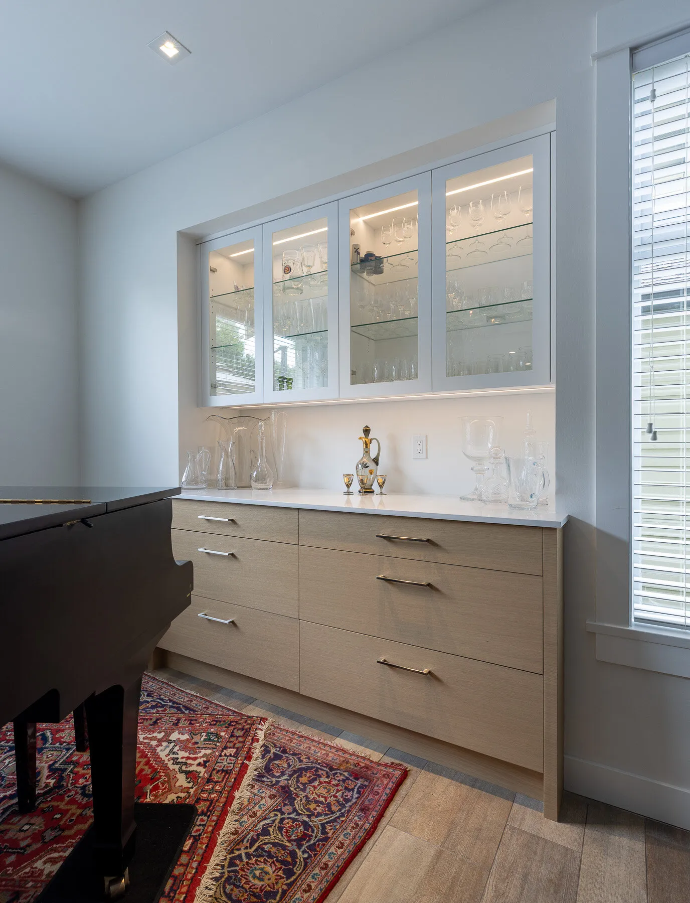 Glass-front china cabinet and wood buffet stand beside the grand piano in the dining room.