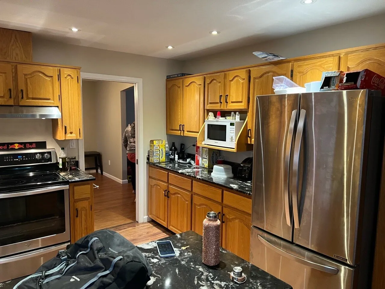 Original kitchen with golden oak cabinets and dark granite counters, cluttered with boxes before renovation.
