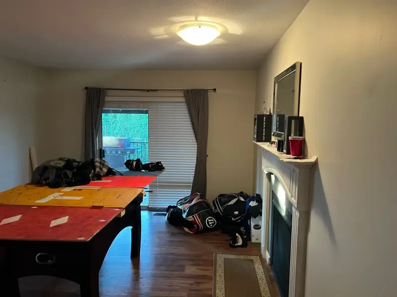 Original living area with a mantel fireplace and sliding glass door, gear piled on the floor pre-renovation.