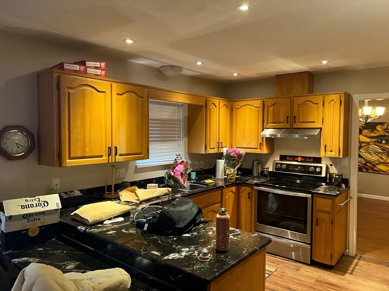 Original kitchen open to the dining room, oak cabinetry and dark granite counters cluttered with moving boxes.