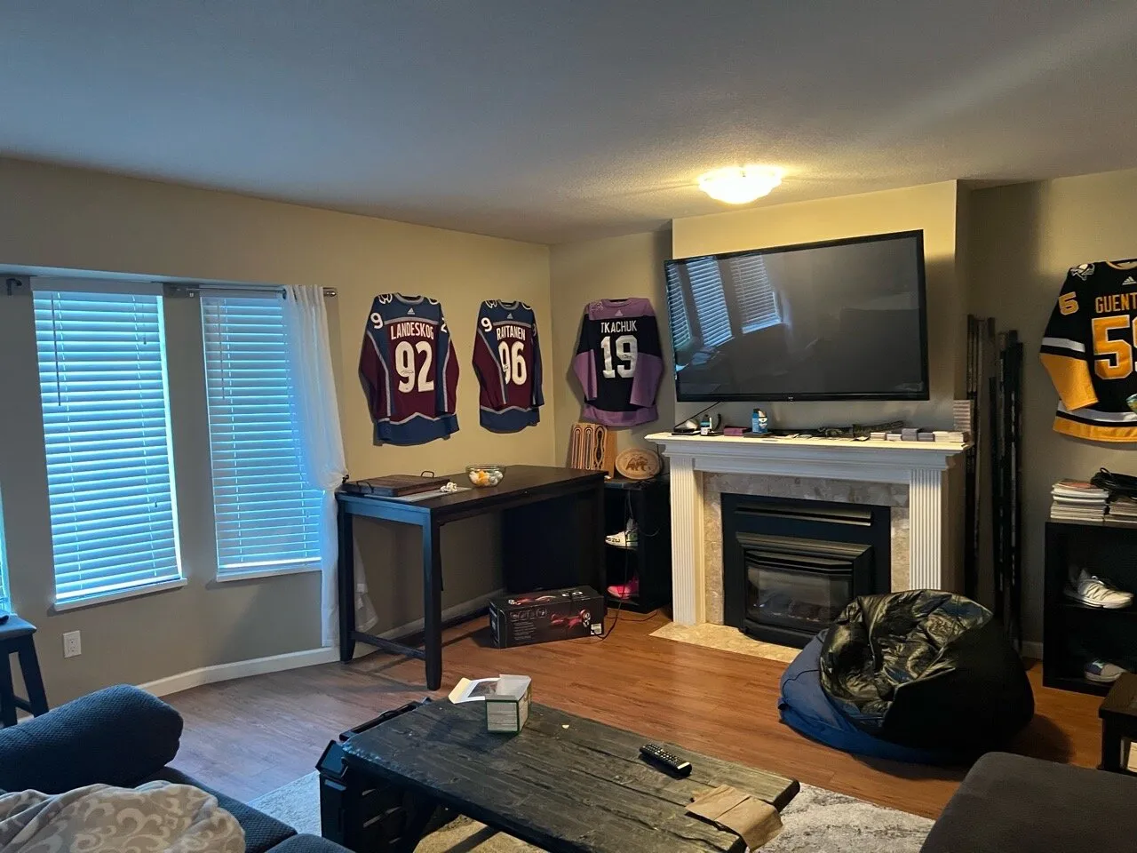 Original living room with hockey jerseys on the walls and a tiled mantel fireplace before renovation.