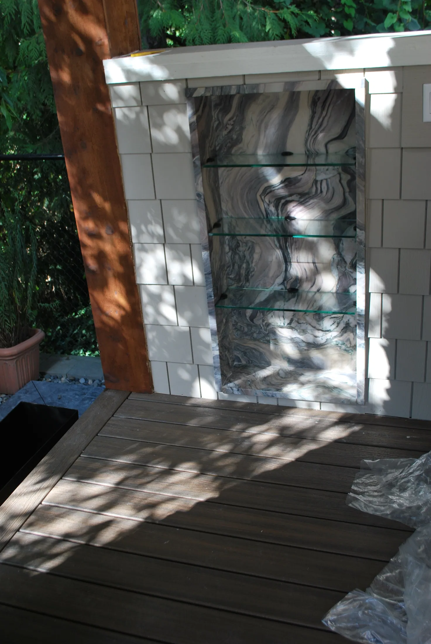 Outdoor display niche under construction with glass shelves and marbled stone backing beside tile.