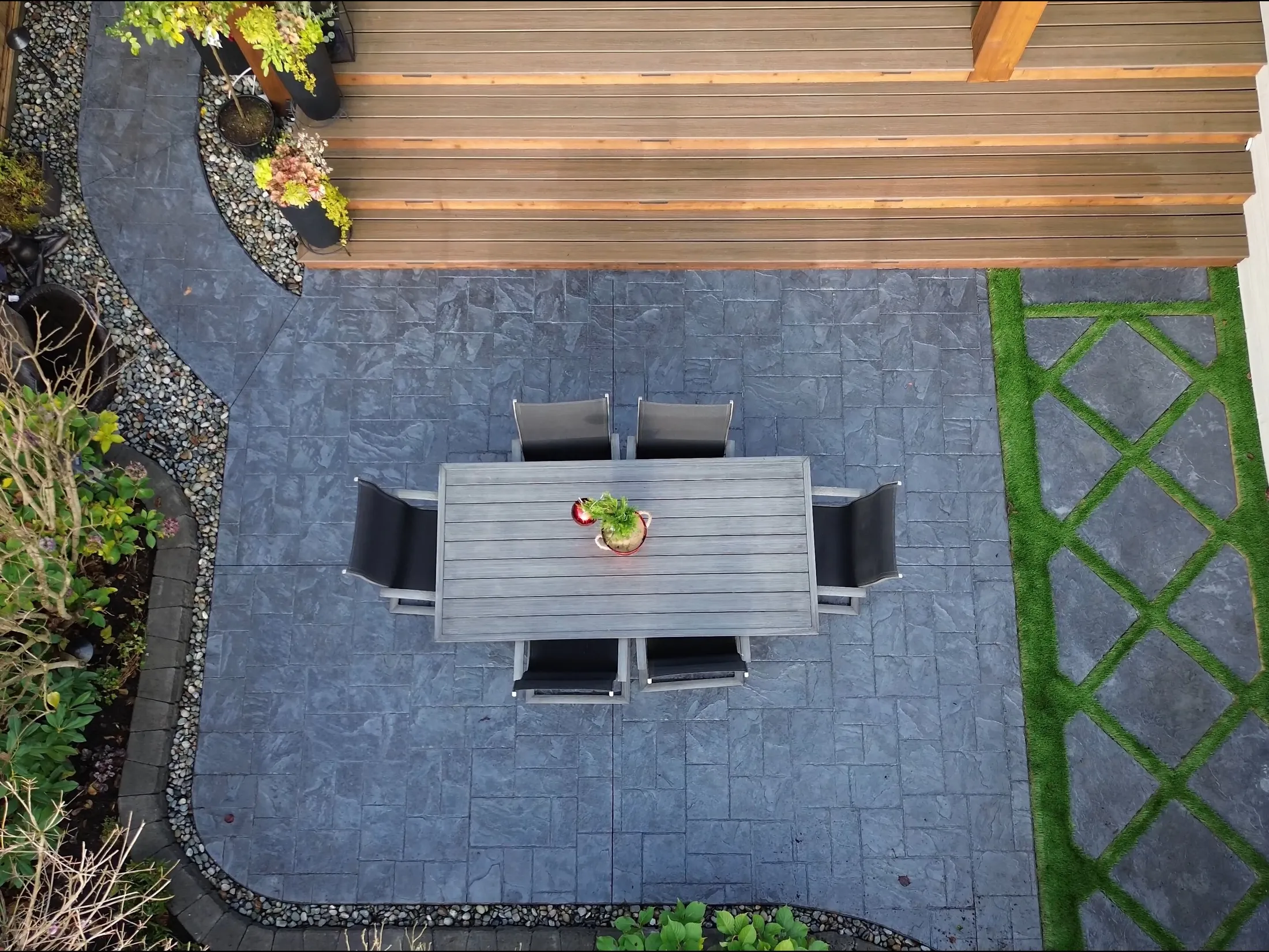 Overhead drone shot looking straight down on the patio dining table, stamped pavers, and turf-lattice inlay.
