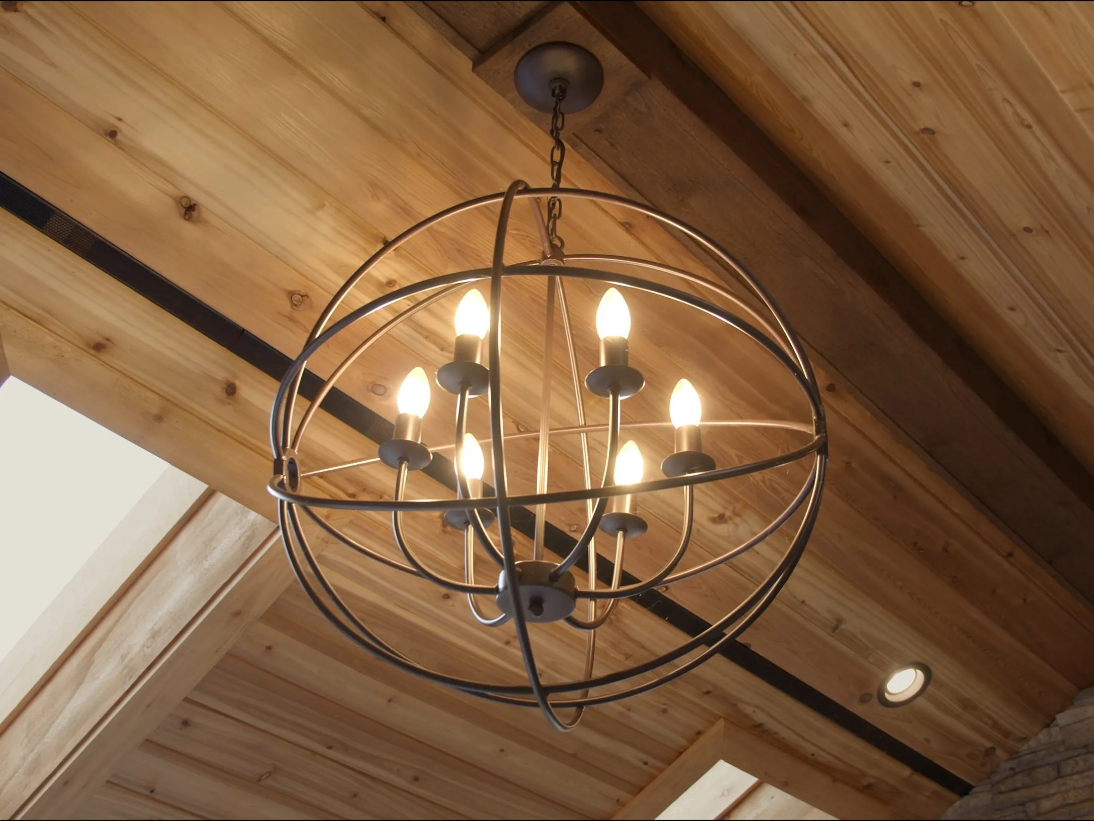 Wrought-iron orb chandelier hanging beneath the vaulted cedar-plank great room ceiling and exposed beams.