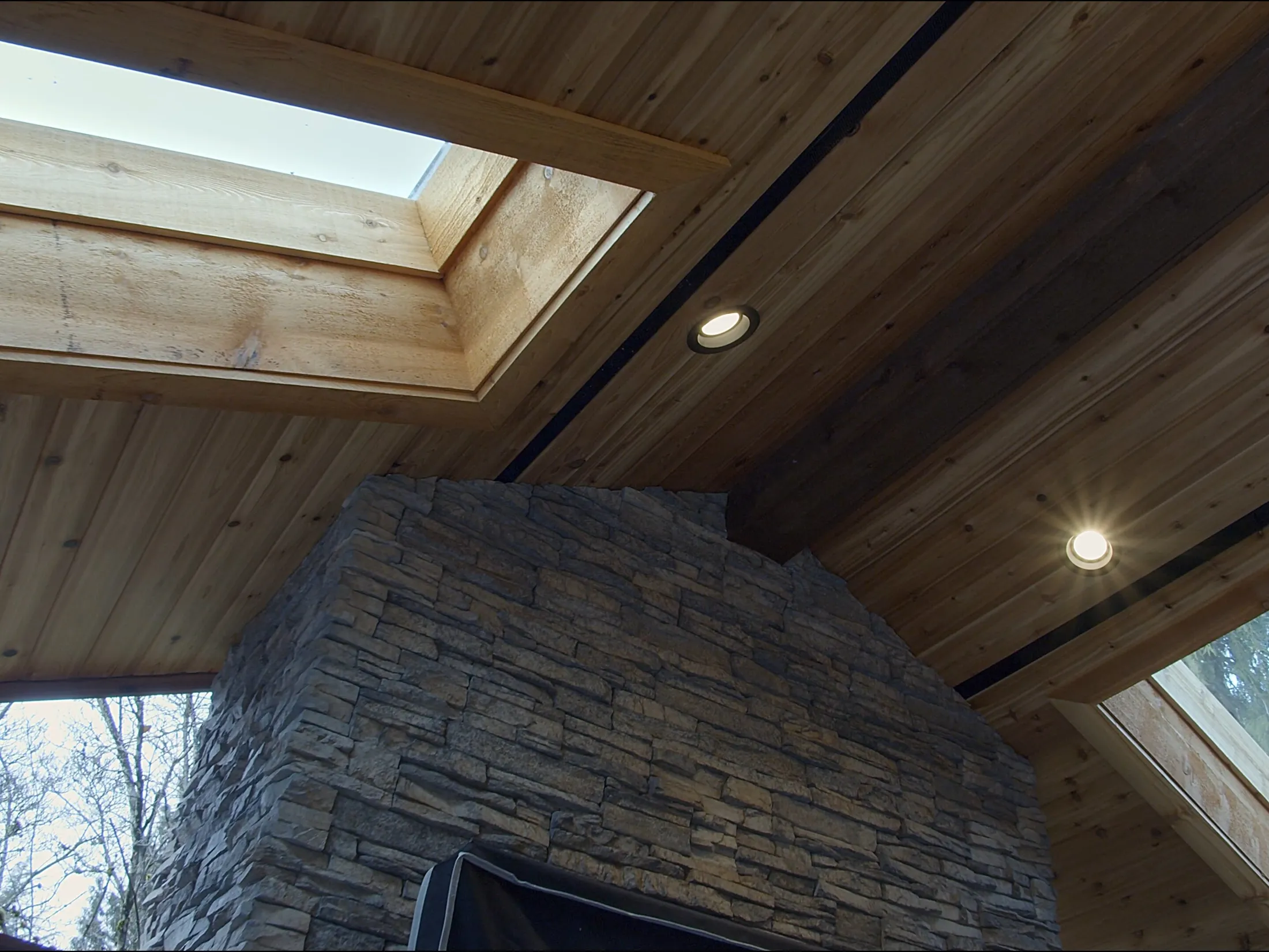 Close-up of the vaulted cedar ceiling, skylight, and stacked-stone chimney meeting overhead.