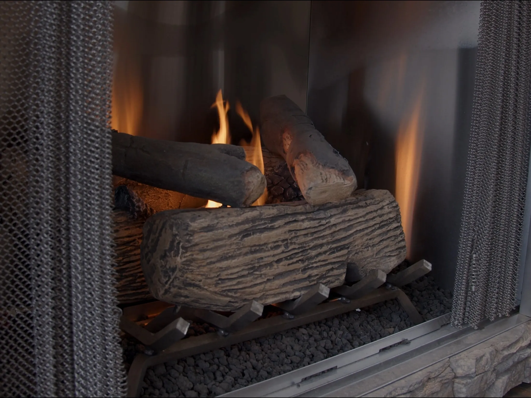 Close-up of the gas fireplace's log set and flame behind the glass screen.