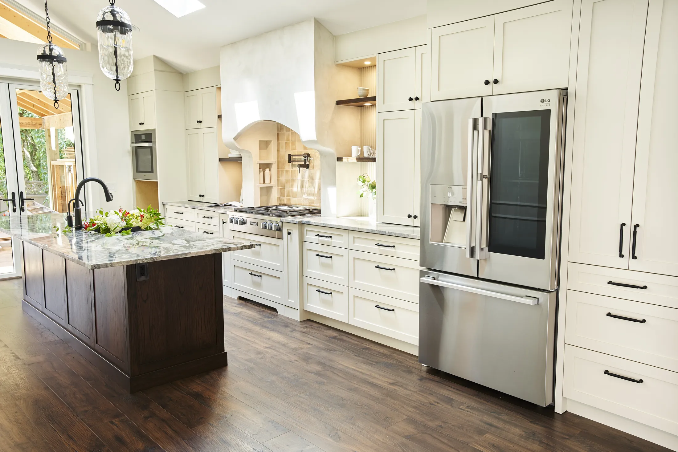 Wide kitchen shot showing the waterfall island, stainless refrigerator, skylights, and French doors to the deck.