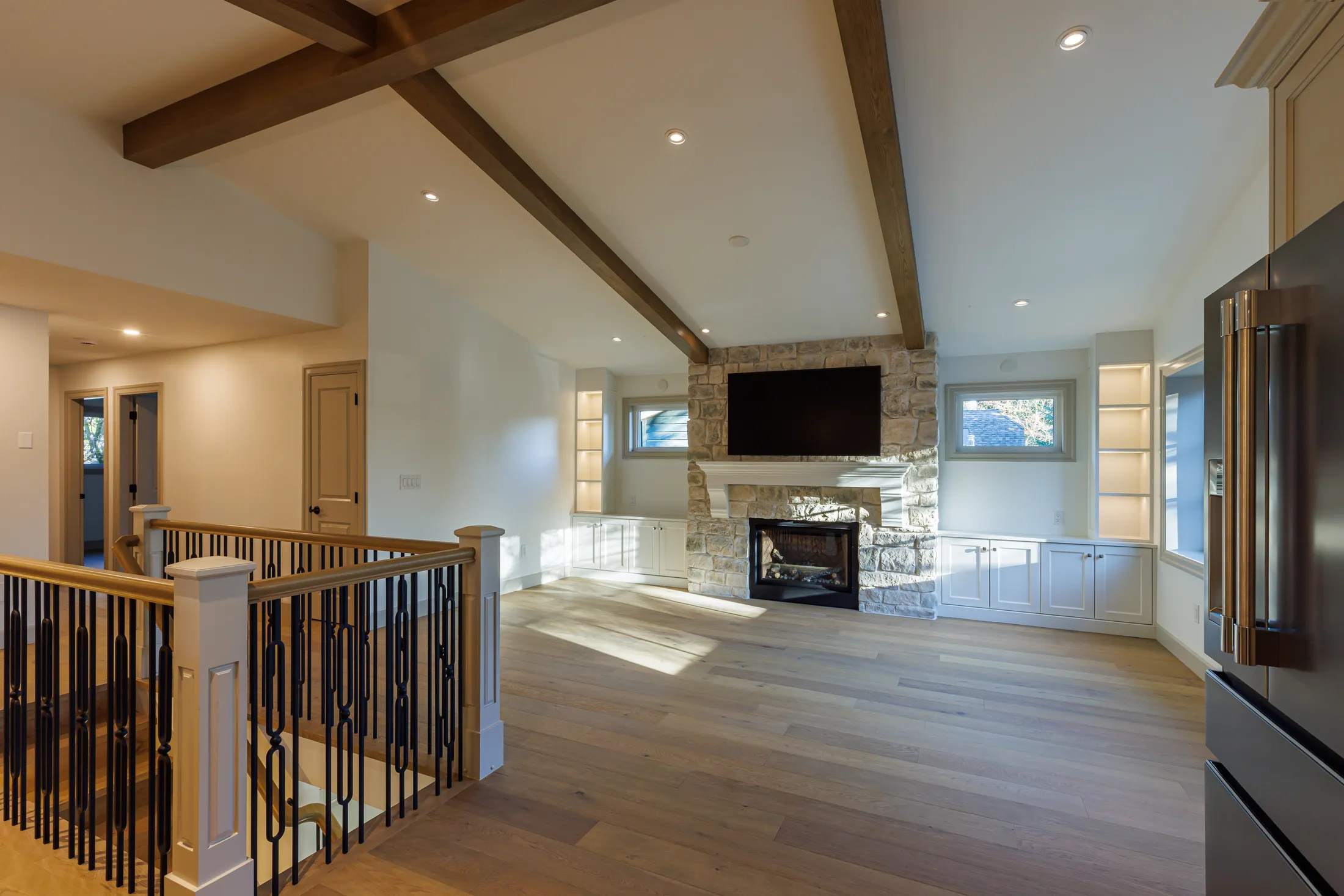 Great room with stone fireplace and mounted TV, seen over the stair railing near the kitchen.