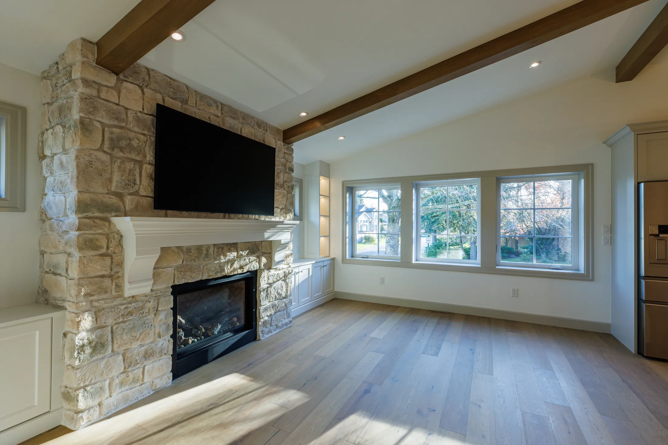 Living room stone fireplace with wood mantel, flanked by a row of windows overlooking the yard.