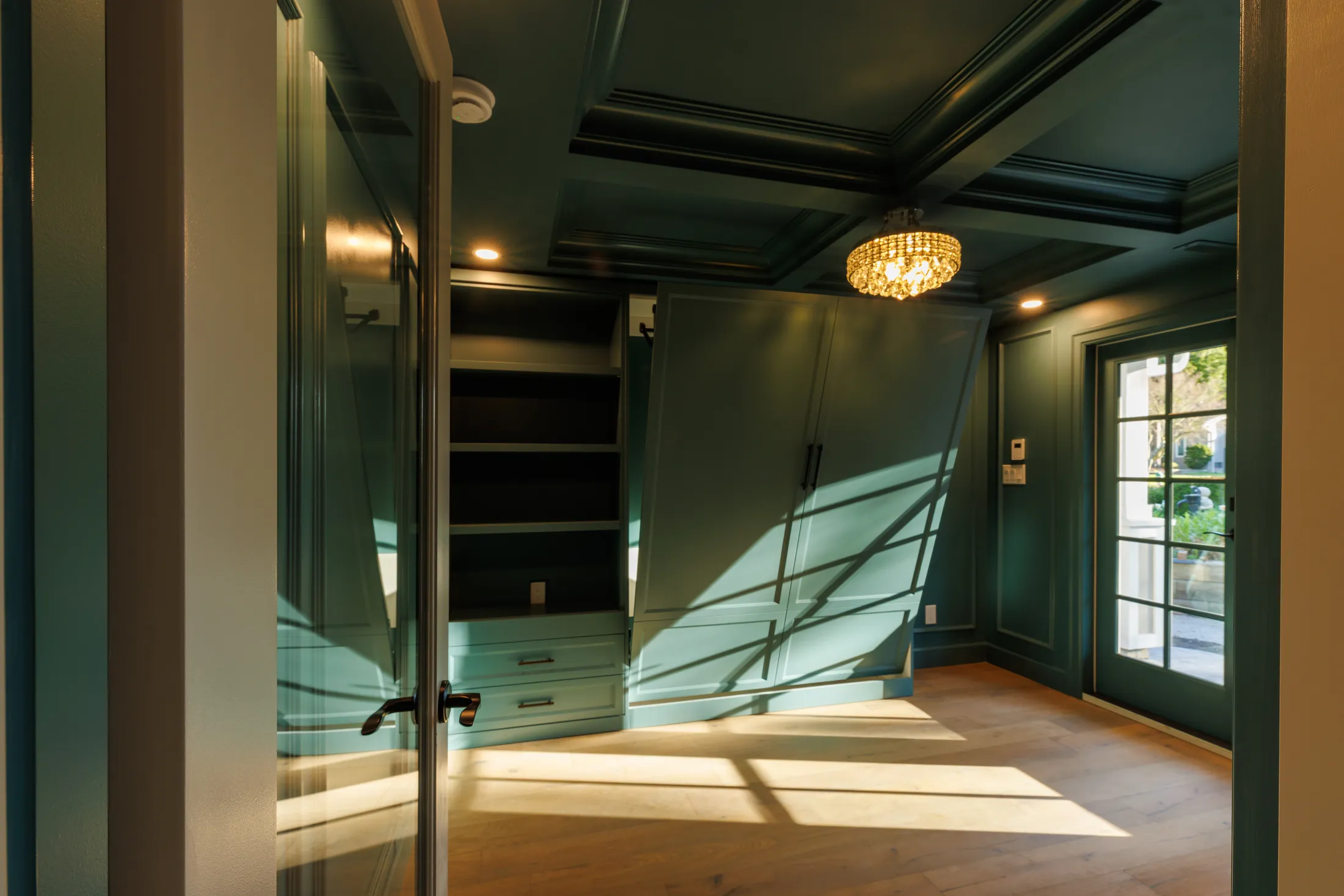 Dark teal dressing room with crystal drum chandelier, coffered ceiling, and built-in wardrobe cabinetry.
