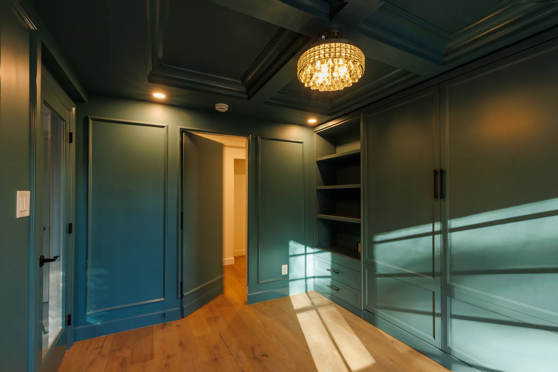 Teal built-in closet with open shelving and paneled wardrobe doors, doorway open to the hallway.
