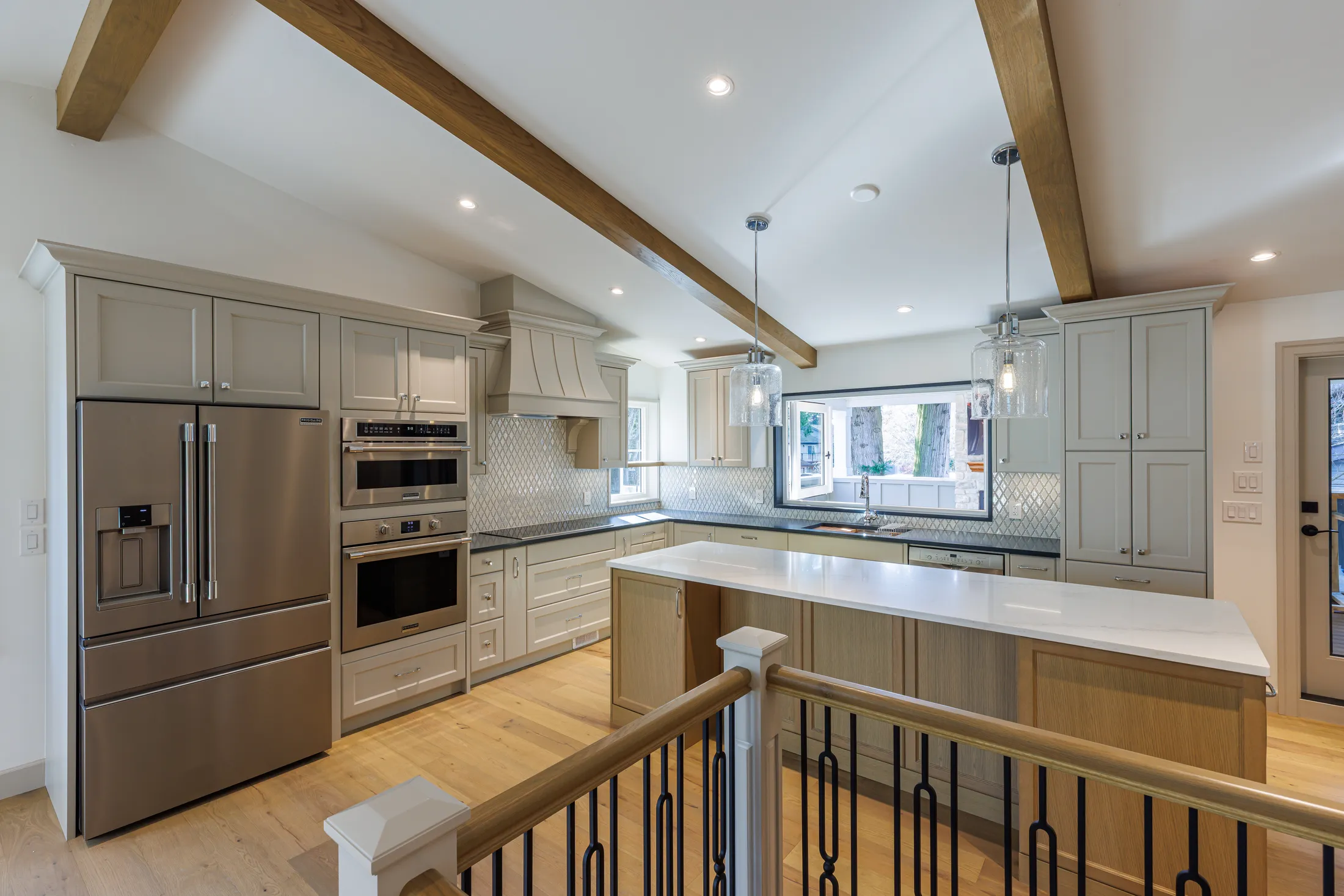 Kitchen with stainless fridge, wall ovens, and island counter overlooking the stairwell railing.