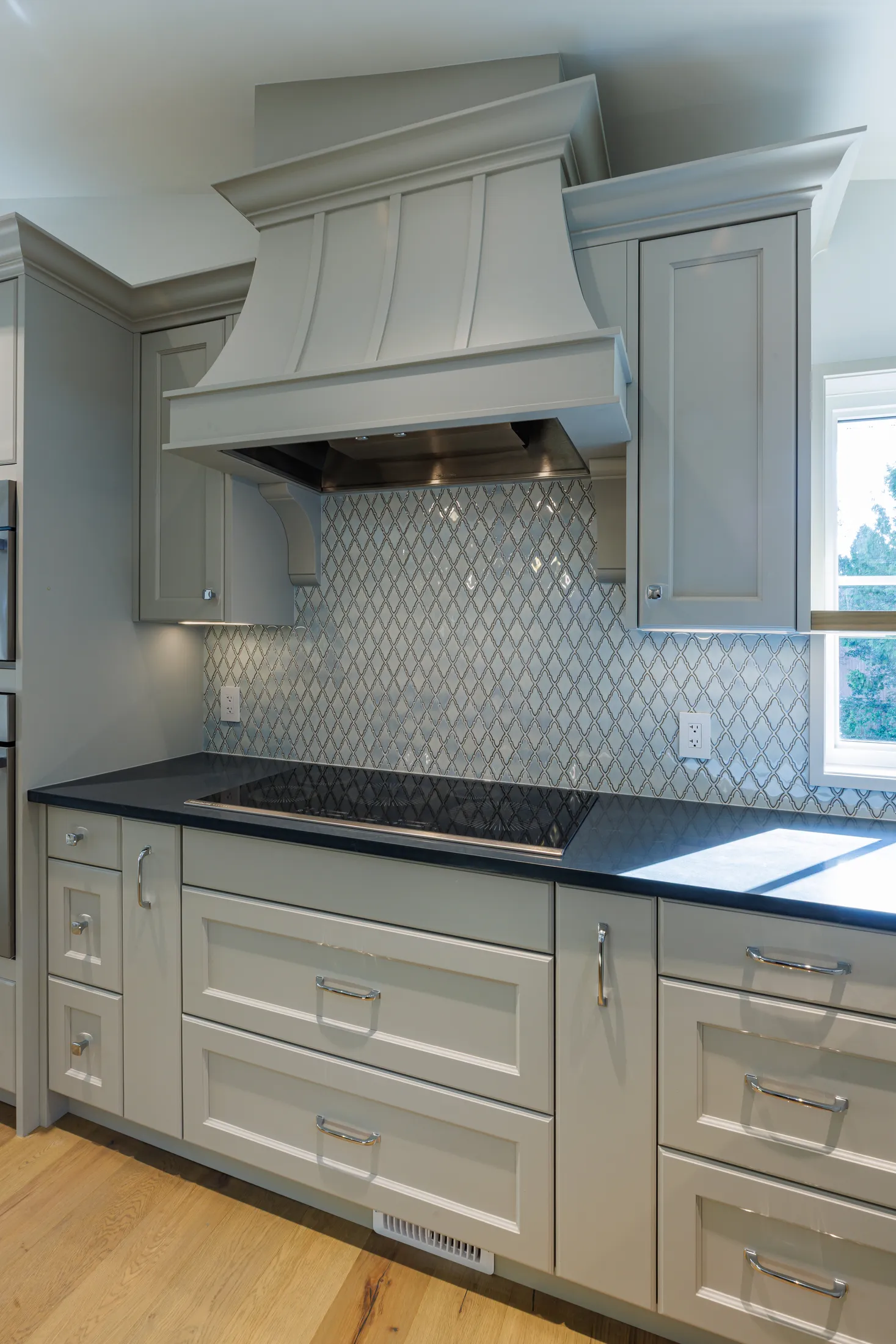 Straight-on view of the pale gray range hood above the cooktop and diamond-patterned tile backsplash.