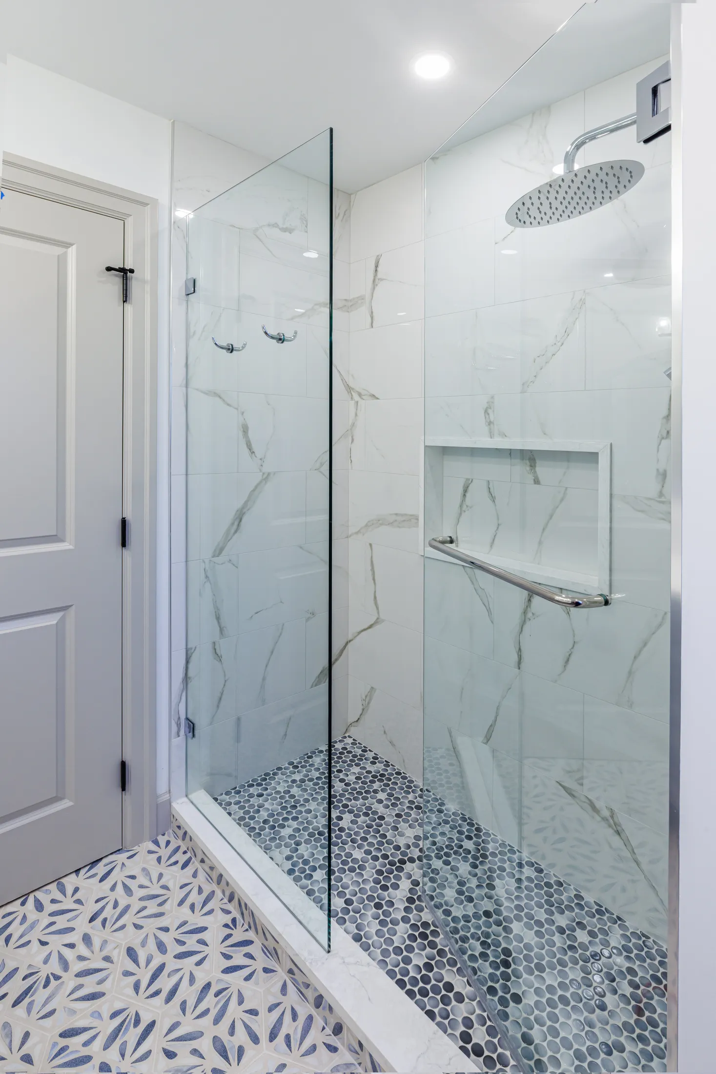 Frameless glass shower with marble subway tile, built-in niche, and dark penny-tile floor.