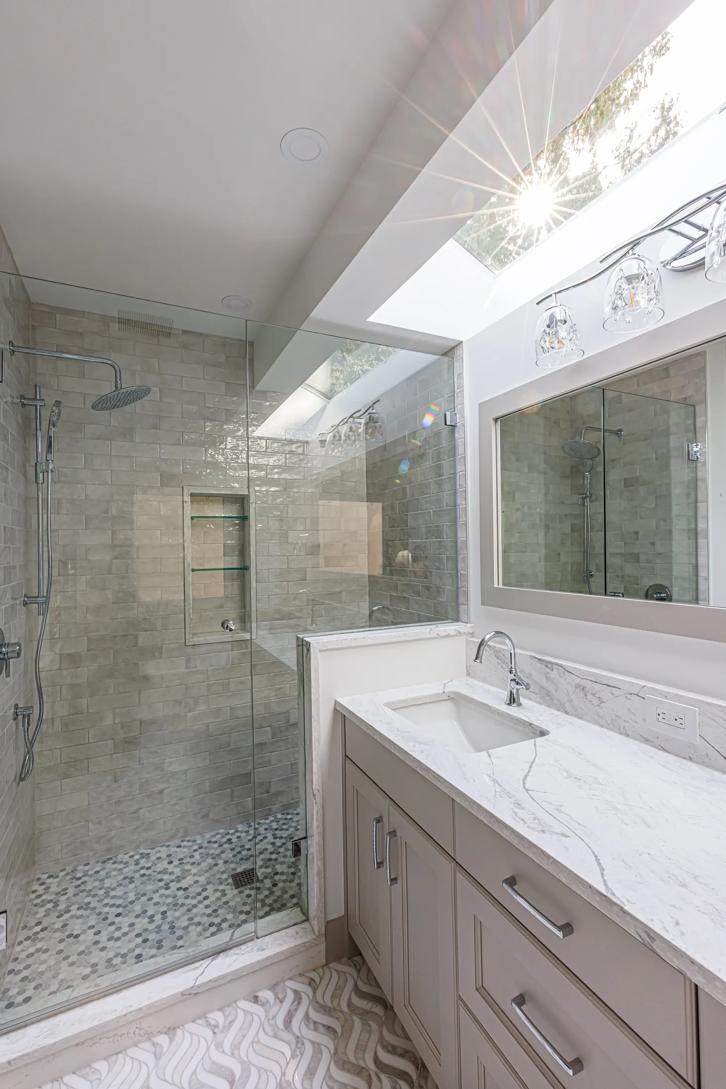 Ensuite bathroom shower with gray subway tile and skylight, plus a marble-top vanity.