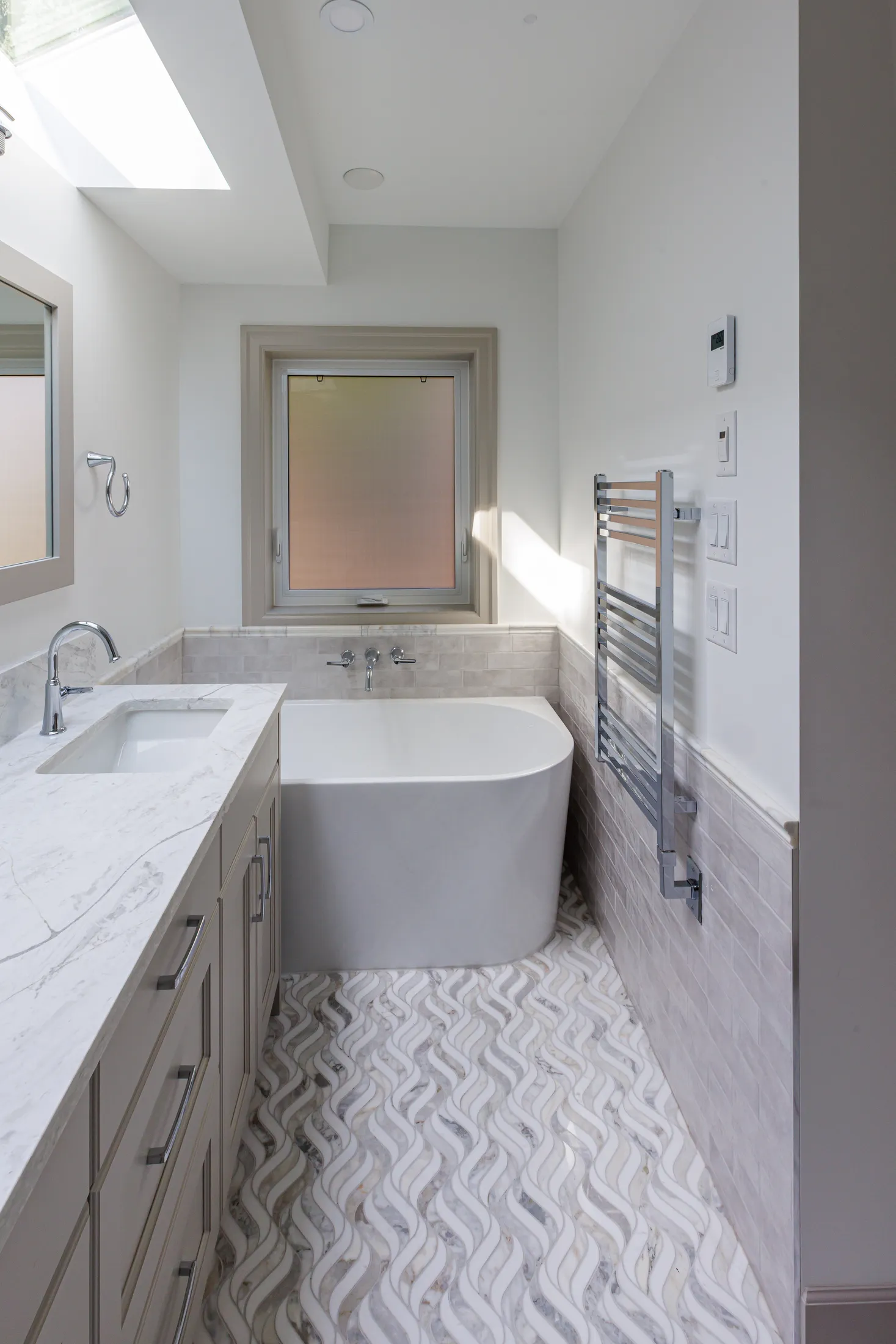 Bathroom with freestanding soaking tub, wall-mount filler, and chrome heated towel rack.