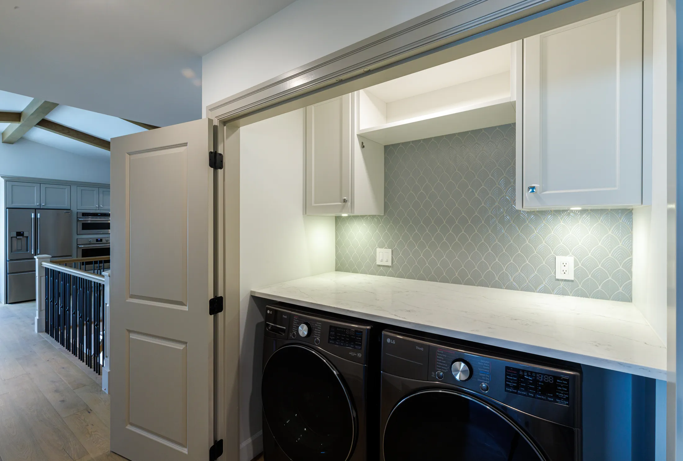 Laundry closet with stacked LG washer and dryer beneath scalloped tile backsplash and cabinets.