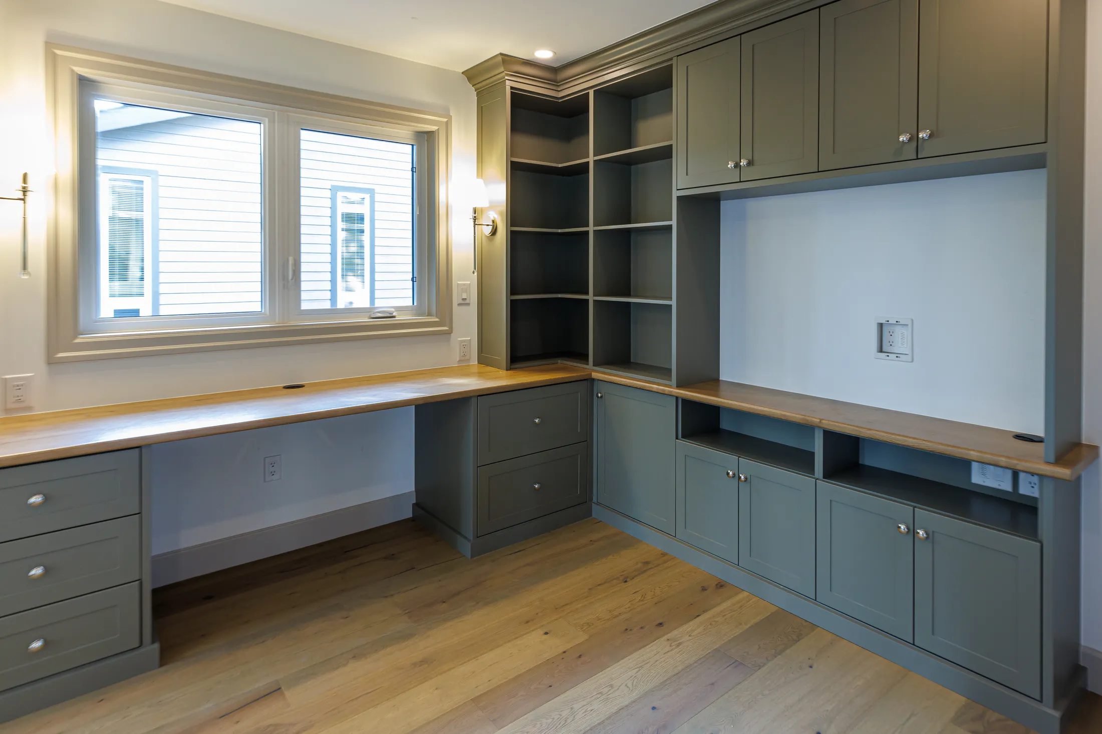 Built-in home office with olive-green cabinetry, open corner shelving, and a wood countertop desk.