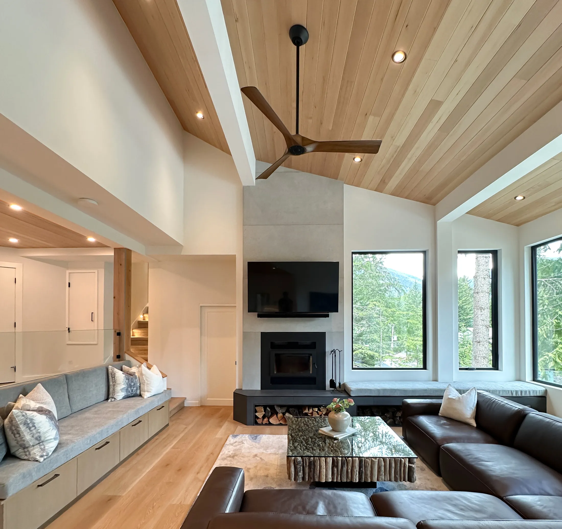 Living room from a second angle: leather sofas, stone coffee table, corner windows framing mountain views.