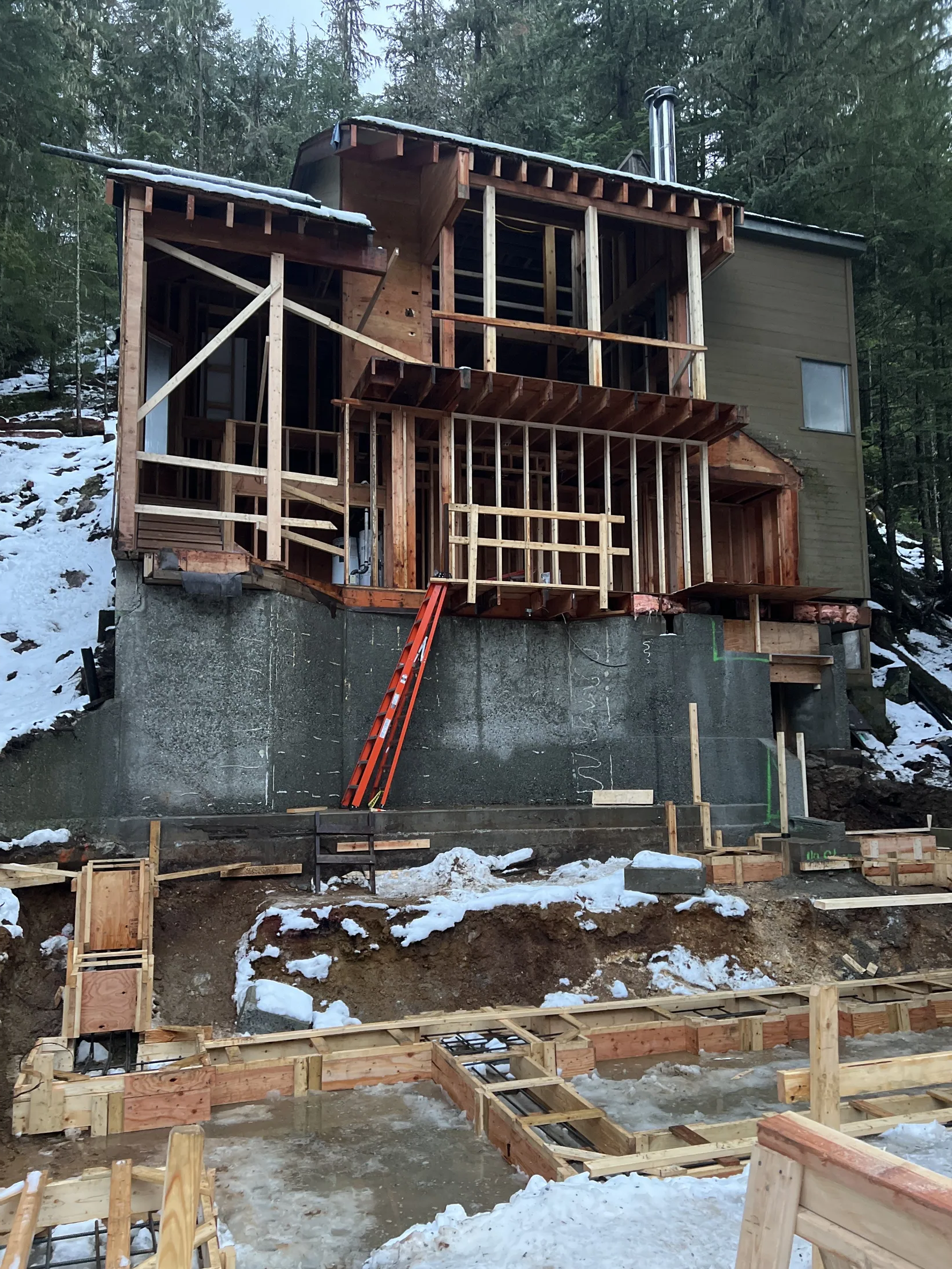 New framing rises above the concrete foundation wall, original siding still attached, snow on the ground.