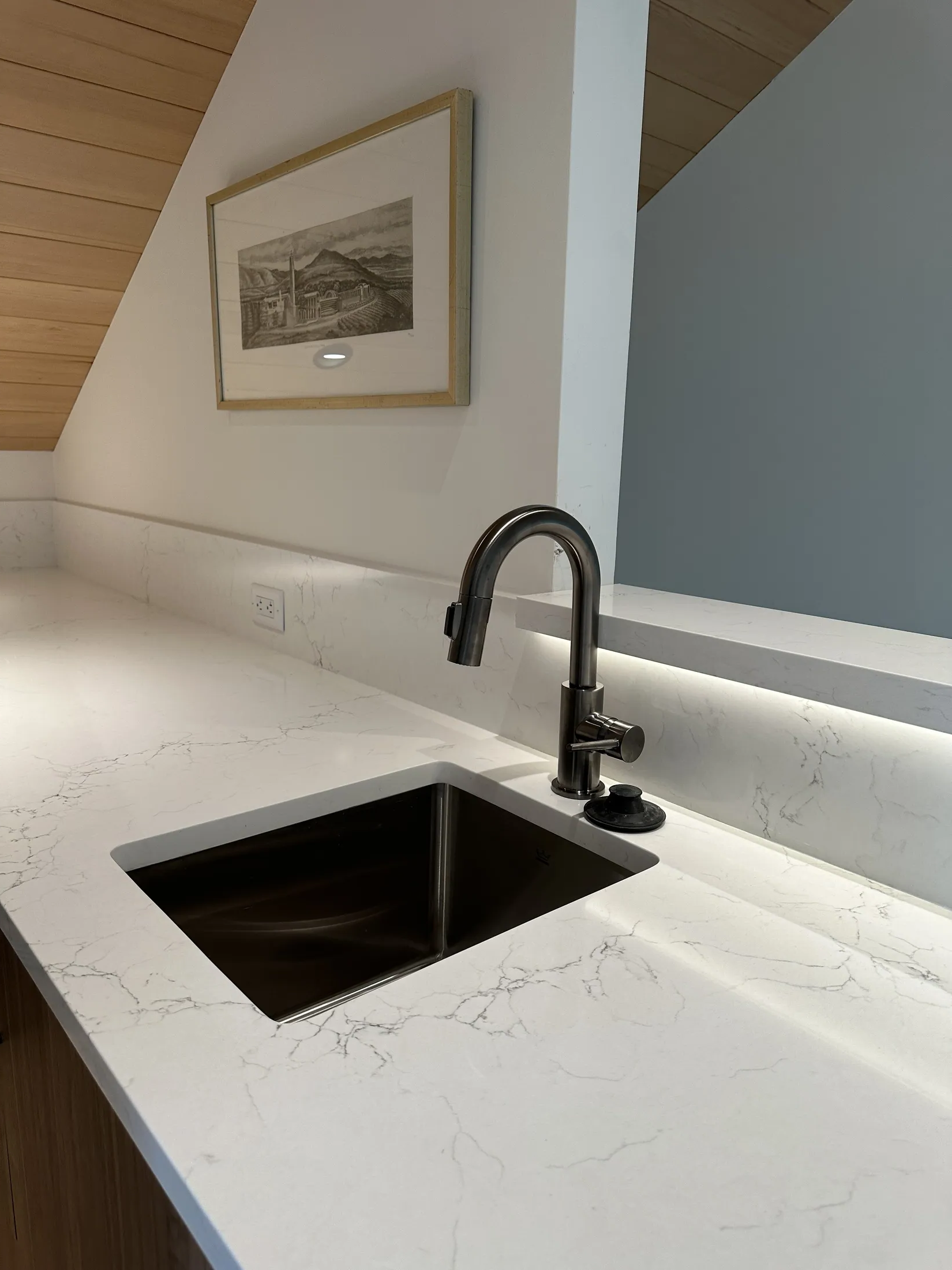 Close-up of the wet bar's undermount sink and gooseneck faucet on quartz counter, framed print above.