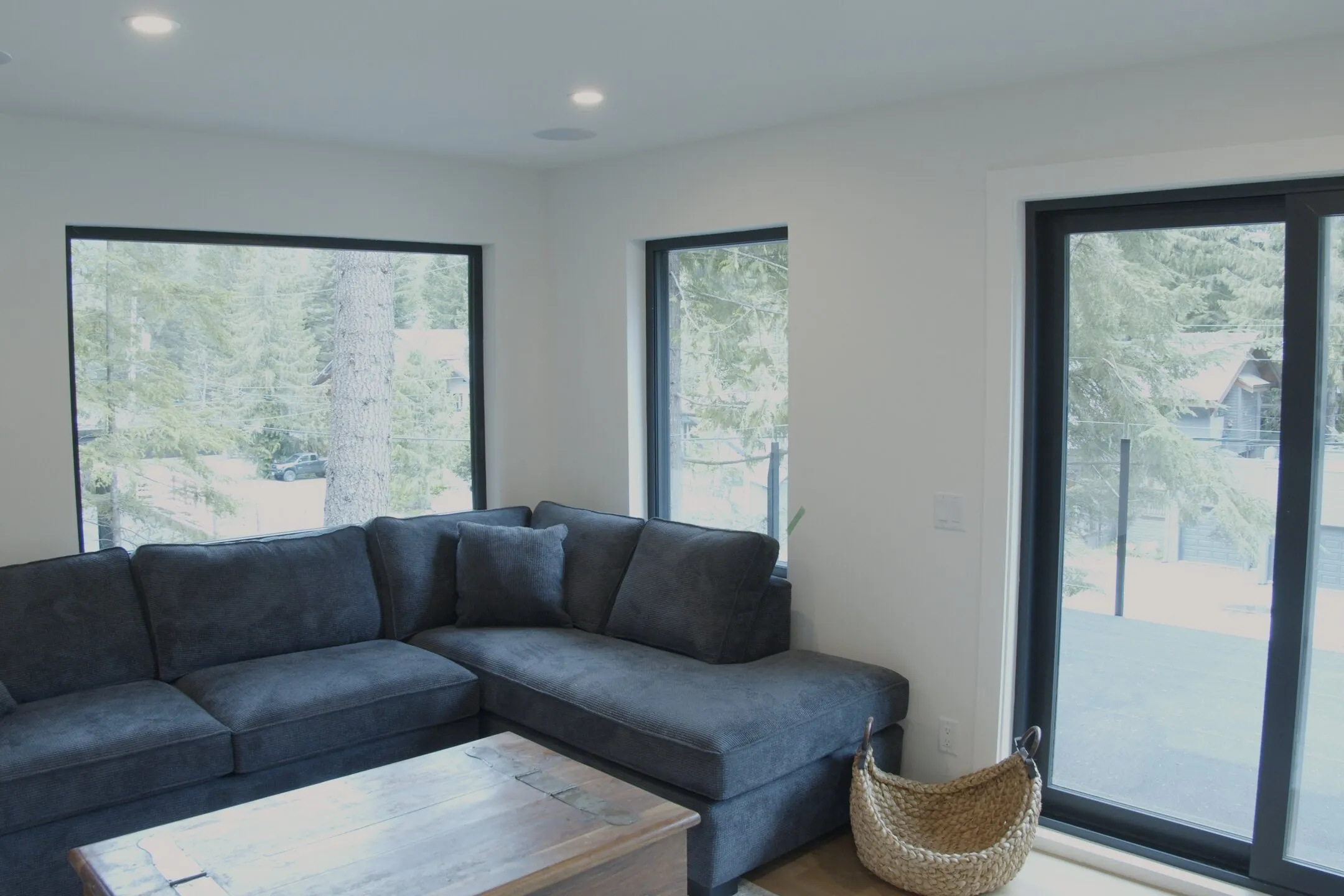 Living room with dark upholstered sectional, reclaimed-wood trunk coffee table, sliding glass door open to deck.