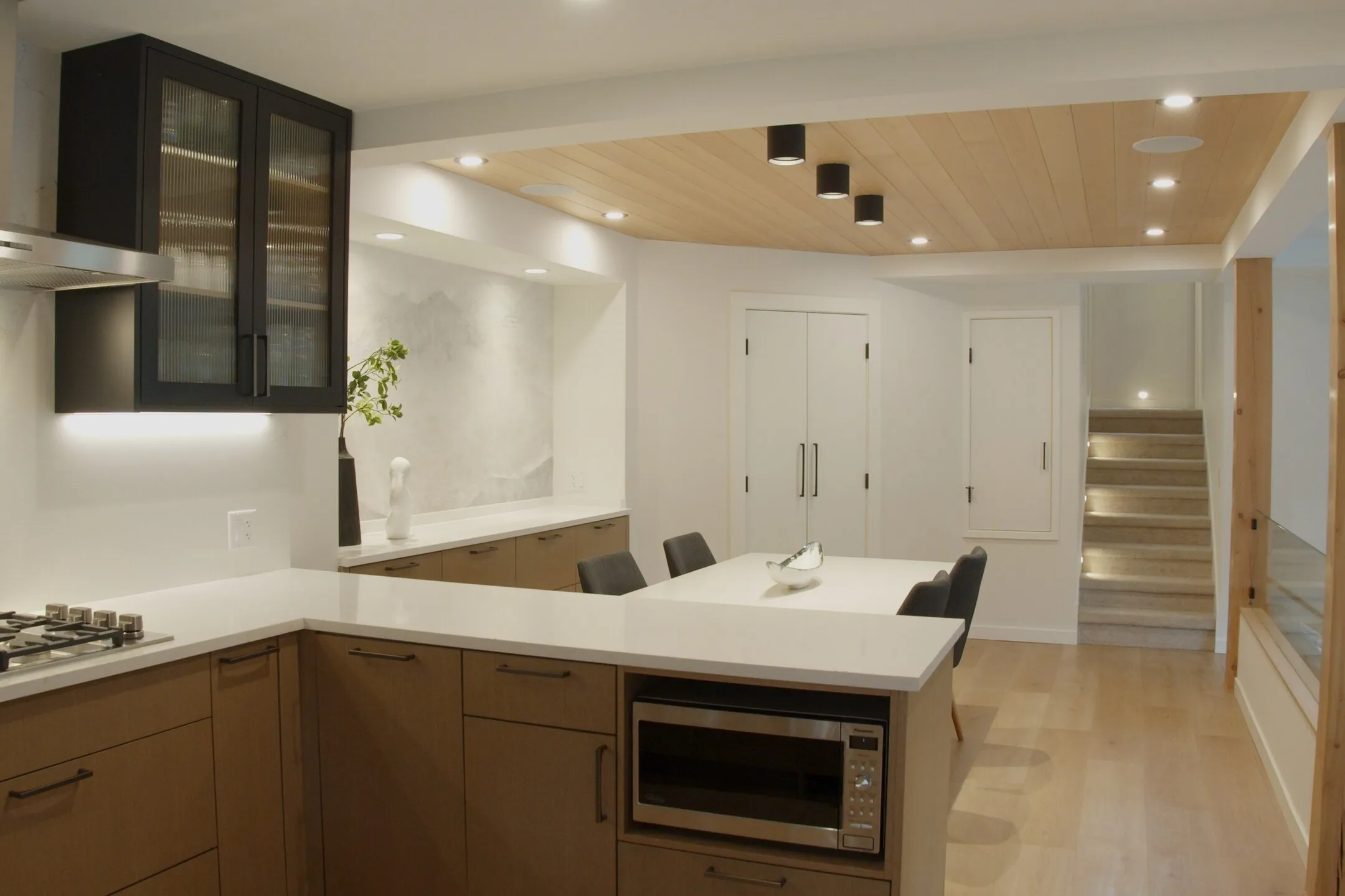 Kitchen and dining area viewed from the stairway, wood-clad ceiling, black cabinetry, staircase leading down.